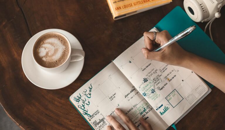 Vista cenital de una persona escribiendo en un diario junto a un café con leche