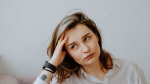 Mujer joven sentada en el sofá con la mano en la cabeza, con gesto de cansancio y preocupación