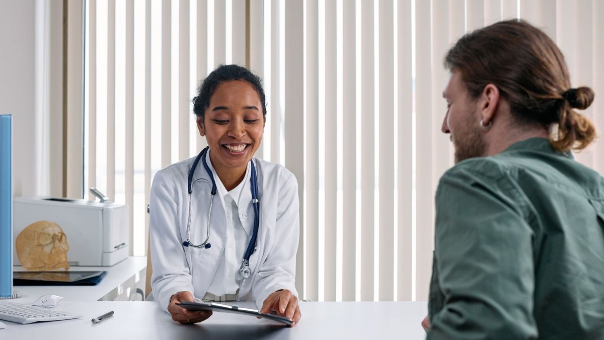 Profesional sanitaria conversando con un paciente al otro lado de la mesa durante una consulta